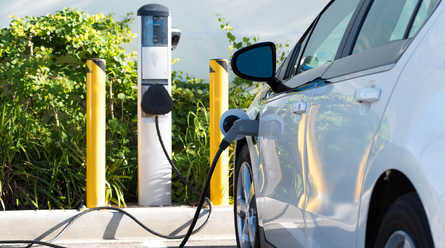 Een persoon sluit een elektrische laadkabel aan op een bedrijfswagen aan een moderne laadpaal in België